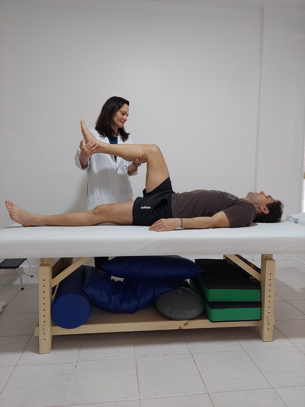Cristiane mobilizando a perna de um paciente na maca